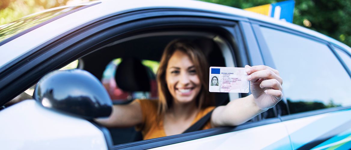 Foto: shutterstock Frau sitzt im Auto und zeigt fröhlich ihren Führerschein.