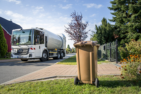 Braune Tonne am Straßenrand - Müllwagen im Hintergrund
